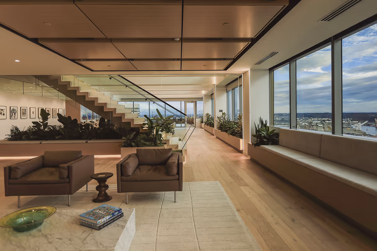 Perkins Coie's office interior with large windows overlooking a city and river, featuring wood floors, glass stairway, indoor plants, and contemporary furniture in a warm, natural-toned design.